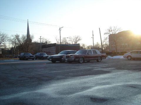 1992 Ford Crown Victoria - Several cars are parked in a lot on a sunny day, with a church steeple visible in the distance.