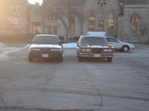 1992 Ford Crown Victoria - Three cars parked in a lot, including a 1992 Ford Crown Victoria.