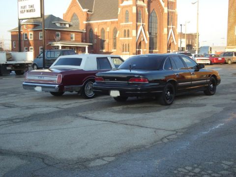1992 Ford Crown Victoria - A black 1992 Ford Crown Victoria is parked next to a maroon car, with a church in the background.