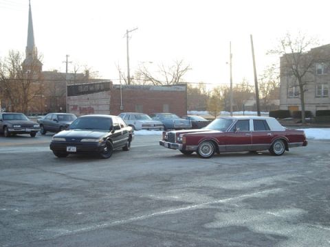 1992 Ford Crown Victoria - Two sedans are parked in a lot with a church steeple in the background.