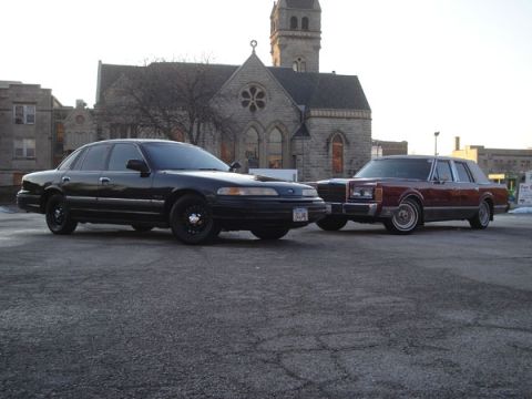1992 Ford Crown Victoria - Two sedans, a black Ford Crown Victoria and a maroon Lincoln Town Car, are parked outside a church.