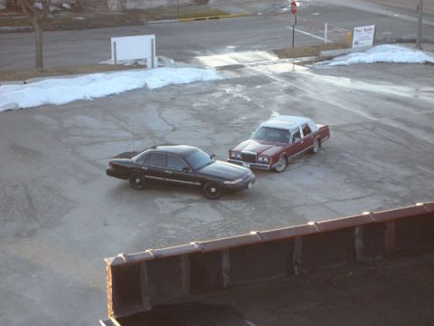 1992 Ford Crown Victoria - Two sedans, a black Ford Crown Victoria and a red Lincoln Town Car, are parked in a lot.