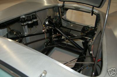 1965 Shelby Cobra - The engine bay of a silver car reveals its internal mechanical structure and suspension system.