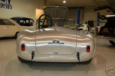 1965 Shelby Cobra - Rear view of a silver sports car with its trunk open, parked in a garage.