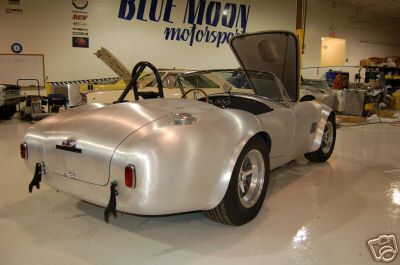 1965 Shelby Cobra - A silver 1965 Shelby Cobra is shown with its hood open in a workshop setting.
