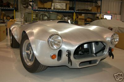 1965 Shelby Cobra - This 1965 Shelby Cobra is captured in a 3/4 front view, its unpainted aluminum body in what appears to be a workshop or storage facility.