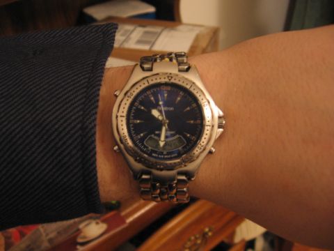 1988 Mercury Grand Marquis - Close-up of a stainless-steel Armitron ana-digi wristwatch with a blue dial and small LCD window, worn on a person's wrist beside a dark pi…