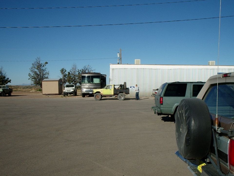 Several vehicles parked in a lot, including a yellow flatbed truck, a green SUV, and an RV