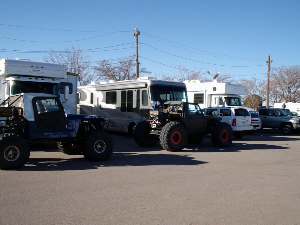 Several custom off-road vehicles parked in front of RVs under a clear blue sky