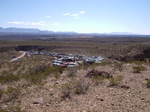1996 Ford Bronco - A vast collection of vehicles are visible in a junkyard, set against a backdrop of distant mountains and a hazy horizon.