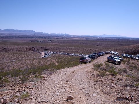 1996 Ford Bronco - A long line of vehicles parked on a dusty, off-road path with a vast landscape in the background.
