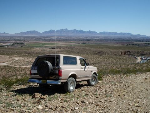 1996 Ford Bronco - Tan Ford Bronco with a spare tire on the back is parked on a rocky incline with a vast landscape in the background.