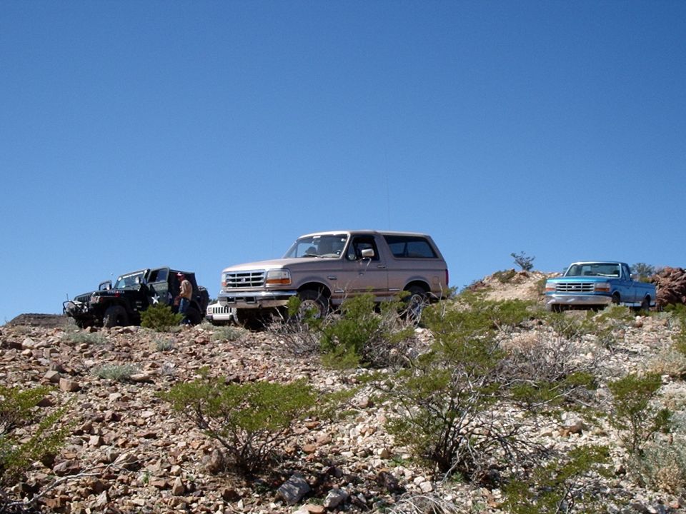 Tan 1996 Ford Bronco 3q-front view on rocky terrain with two other vehicles