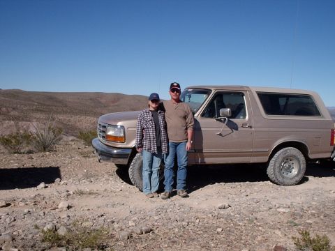 1996 Ford Bronco - Two people pose with a tan Ford Bronco in a desert setting under a clear blue sky.