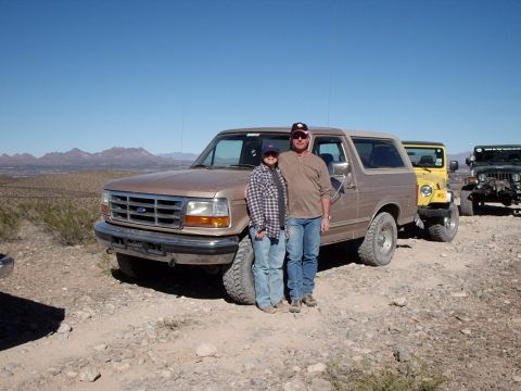 1996 Ford Bronco - A couple poses with their Ford Bronco in a desert landscape, with other off-road vehicles nearby.