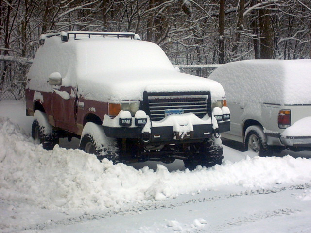 Snow-covered red and gray SUV with brush guard parked outdoors