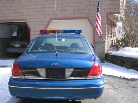 1991 Ford Crown Victoria LTD - Rear view of a blue police car with a light bar parked outside a garage in the snow.