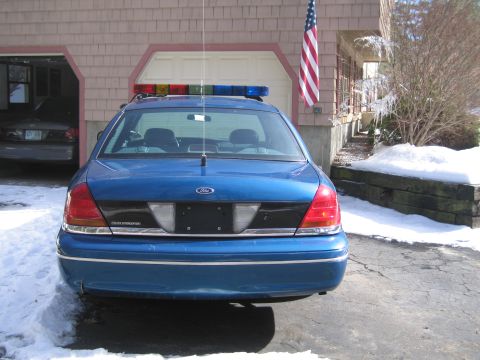 1991 Ford Crown Victoria LTD - A blue police car is parked in front of a garage with an American flag displayed.