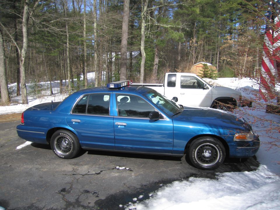 Blue police sedan with light bar on roof, parked next to a white pickup truck
