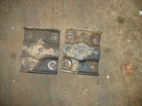 1992 Ford Mustang - Two used metal brackets with visible rust and wear are displayed on a rough surface.