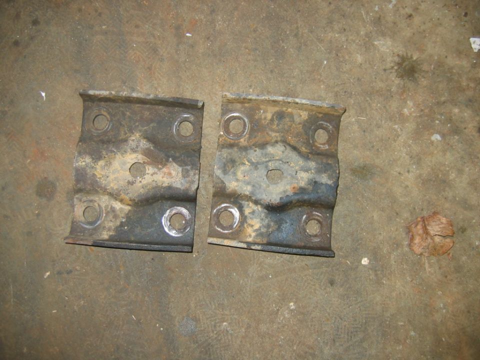 Two rusty, rectangular metal brackets with four bolt holes each, lying on a concrete floor