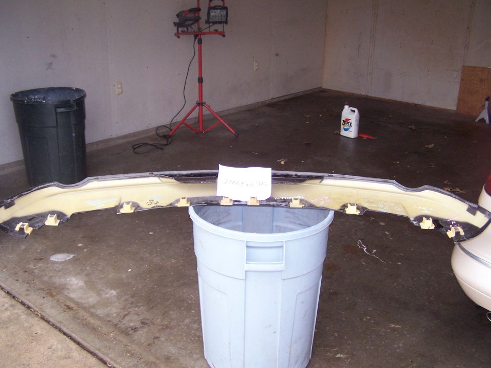 Front bumper fascia resting on trash cans in a garage