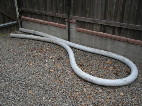 1990 Ford Bronco - Two large flexible hoses are coiled on the ground next to a fence and a concrete retaining wall.