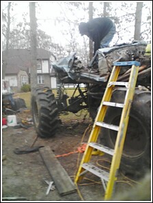 2004 Jeep Wrangler - A person works on a custom-built, oversized off-road vehicle with massive tires in a yard.