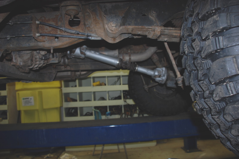 Driveshaft and rear suspension of a vehicle on a lift, showing rust and wear