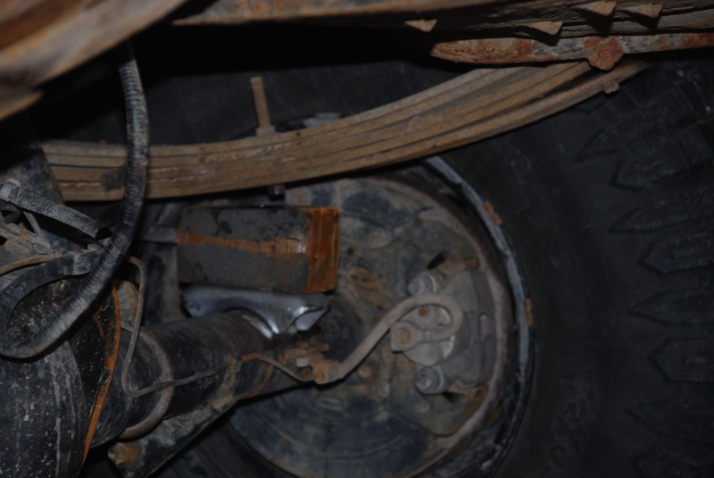 Rear axle, leaf springs, and brake drum assembly of a vehicle, showing rust and wear