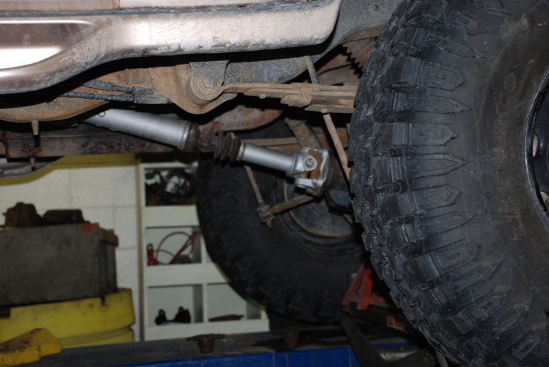 Underside view of a vehicle's driveshaft, U-joint, leaf spring, and tire