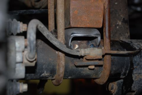 1996 Ford Bronco - Detail of a vehicle's rear axle suspension system, showing a rusty metal bracket and brake line.