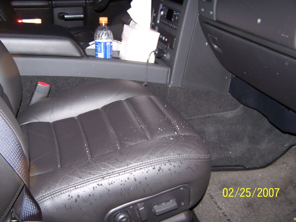 Black leather car seat with water spots, center console with bottle and tissues, date stamp 02/25/2007