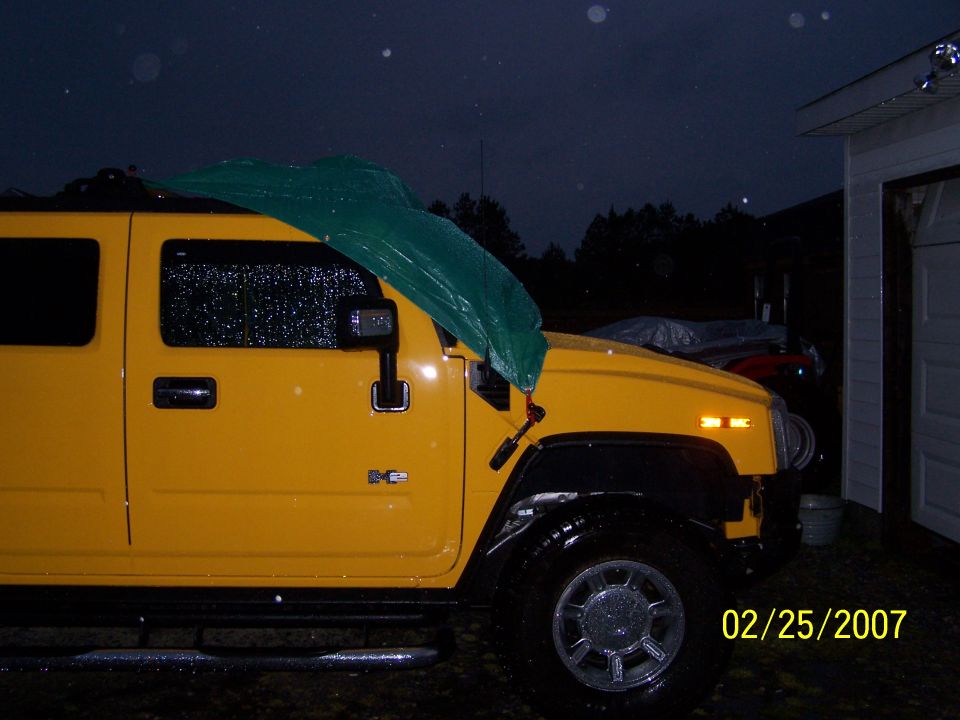 Yellow Hummer H2 at night with a green tarp bungeed over the windshield in the rain