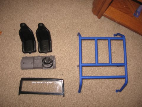 1990 Ford Bronco - Model car parts including seats, dashboard, steering wheel, windshield, and a blue roll cage are laid out on a carpeted surface.