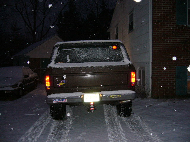 Rear view of a brown Ford Bronco parked in the snow. Another car is visible to the left