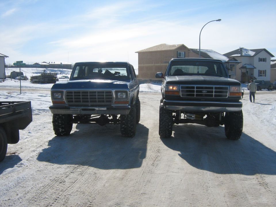 two lifted Ford trucks parked in snow, one blue, one black