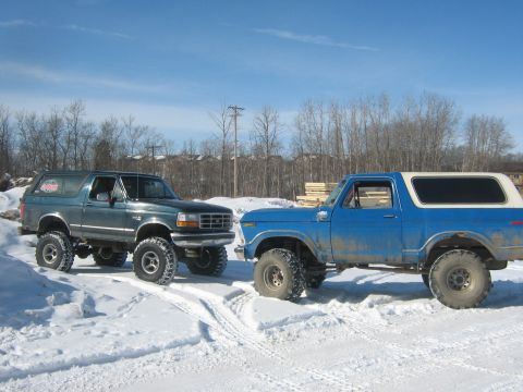 1995 Ford Bronco - Two Ford Broncos, one from the late 1970s and another from the mid-1990s, parked in a snowy landscape.