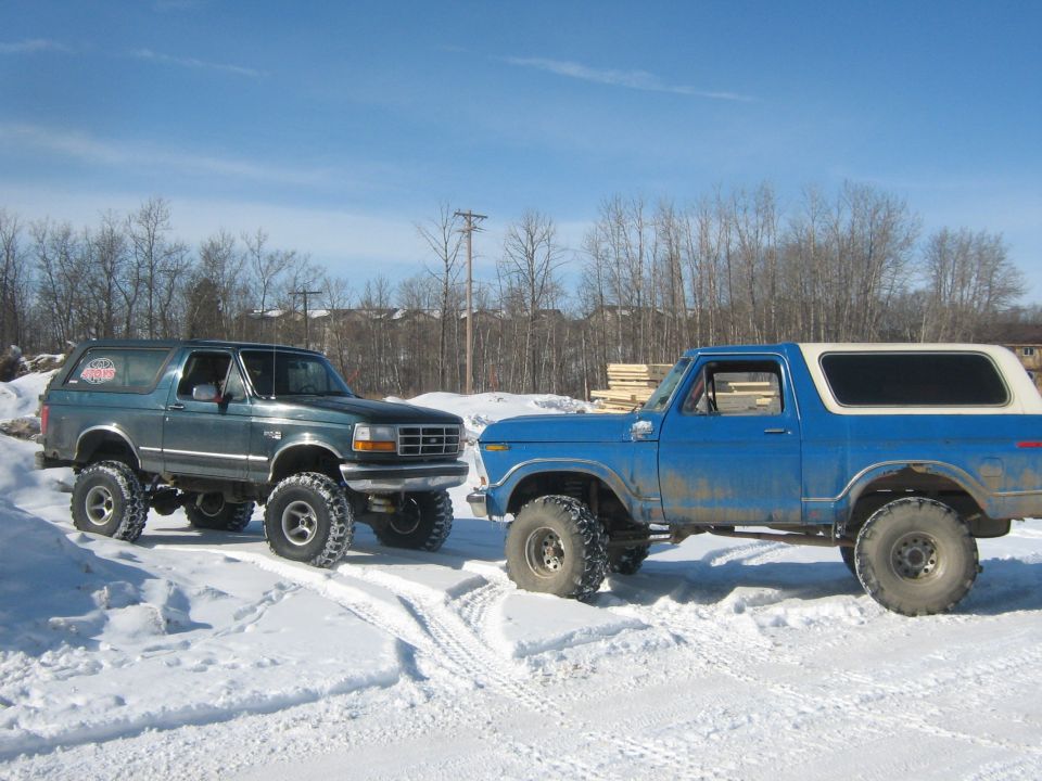 Two lifted Ford Broncos in the snow; one is green and black, the other is blue with a white top