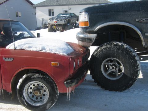 1995 Ford Bronco - A red Toyota Hilux is seen in a close encounter with a lifted dark green Ford Bronco in a snowy environment.