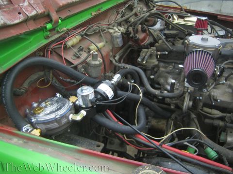 1987 Suzuki Samurai - Engine bay features a propane conversion kit, including a regulator and various hoses, with visible wiring and engine components.