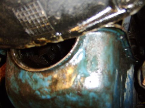 1989 Ford Bronco - Extreme close-up of an oily engine component, showing a hex-shaped bolt head recessed in a dark opening, surrounded by teal/blue and rust-s…