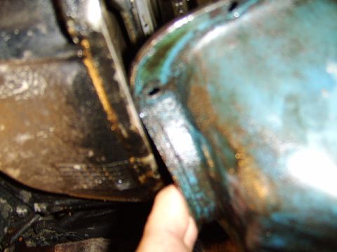 1989 Ford Bronco - Close-up of a greenish-blue painted engine oil pan and its mating surface, with visible grime, oil residue and surface rust, and a person's…