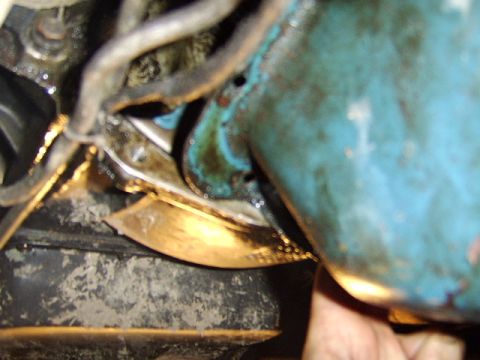1989 Ford Bronco - Close-up under a vehicle showing a teal/blue-green painted component next to an oil pan area, with hoses, wiring, and greasy metal surfaces…