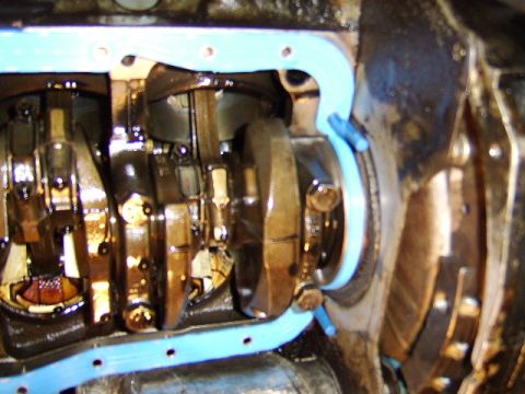 1989 Ford Bronco - Underside view of an engine block with the oil pan removed, showing the crankshaft, connecting rod journals, and main bearing caps. A light…