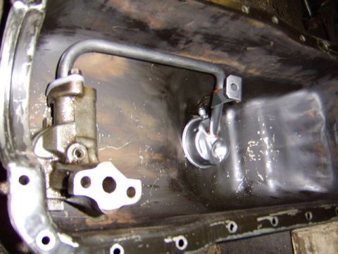 1989 Ford Bronco - Close-up of an engine oil pump and pickup tube assembly mounted to the lower block, with the oil pan removed exposing bare metal and a moun…