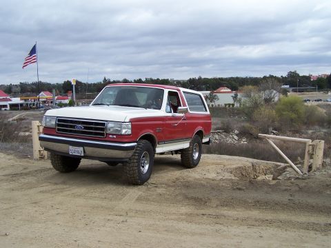 1989 Ford Bronco - This two-tone red and white 1989 Ford Bronco is parked on a dirt road with an American flag flying nearby.