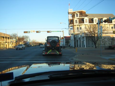 1996 Ford Bronco - A Jeep Wrangler is transported on a trailer through a town intersection under a clear sky.