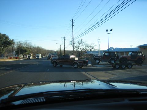 1996 Ford Bronco - A Ford F-250 pickup truck tows a trailer carrying two Jeep SUVs down a suburban street.
