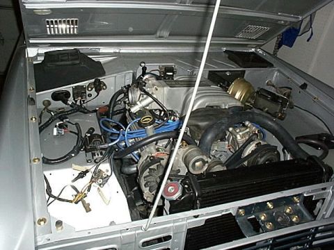 1986 Ford Bronco - The engine bay of a 1986 Ford Bronco shows a V8 engine with extensive wiring and hoses.